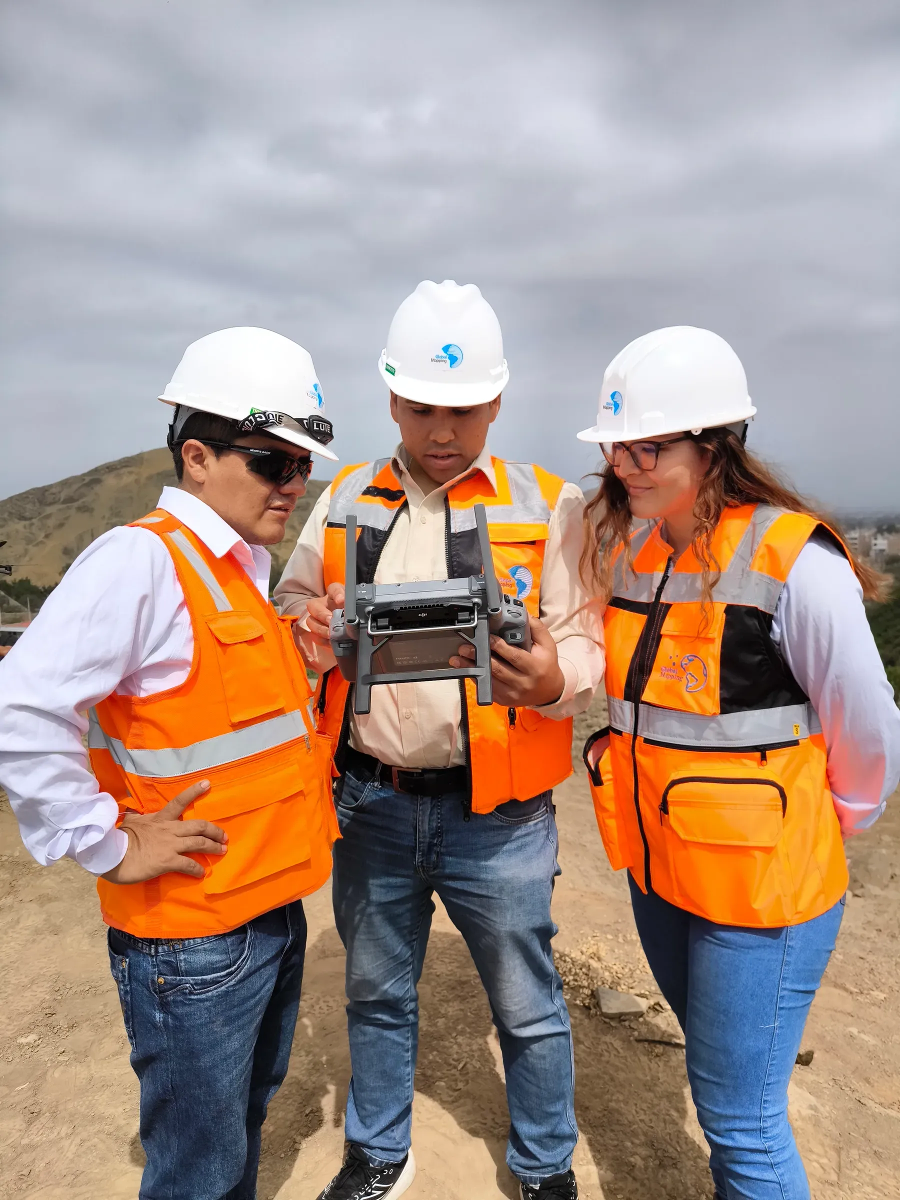 Tres especialistas de Global Mapping con casco y chaleco revisan en campo el control remoto de un dron