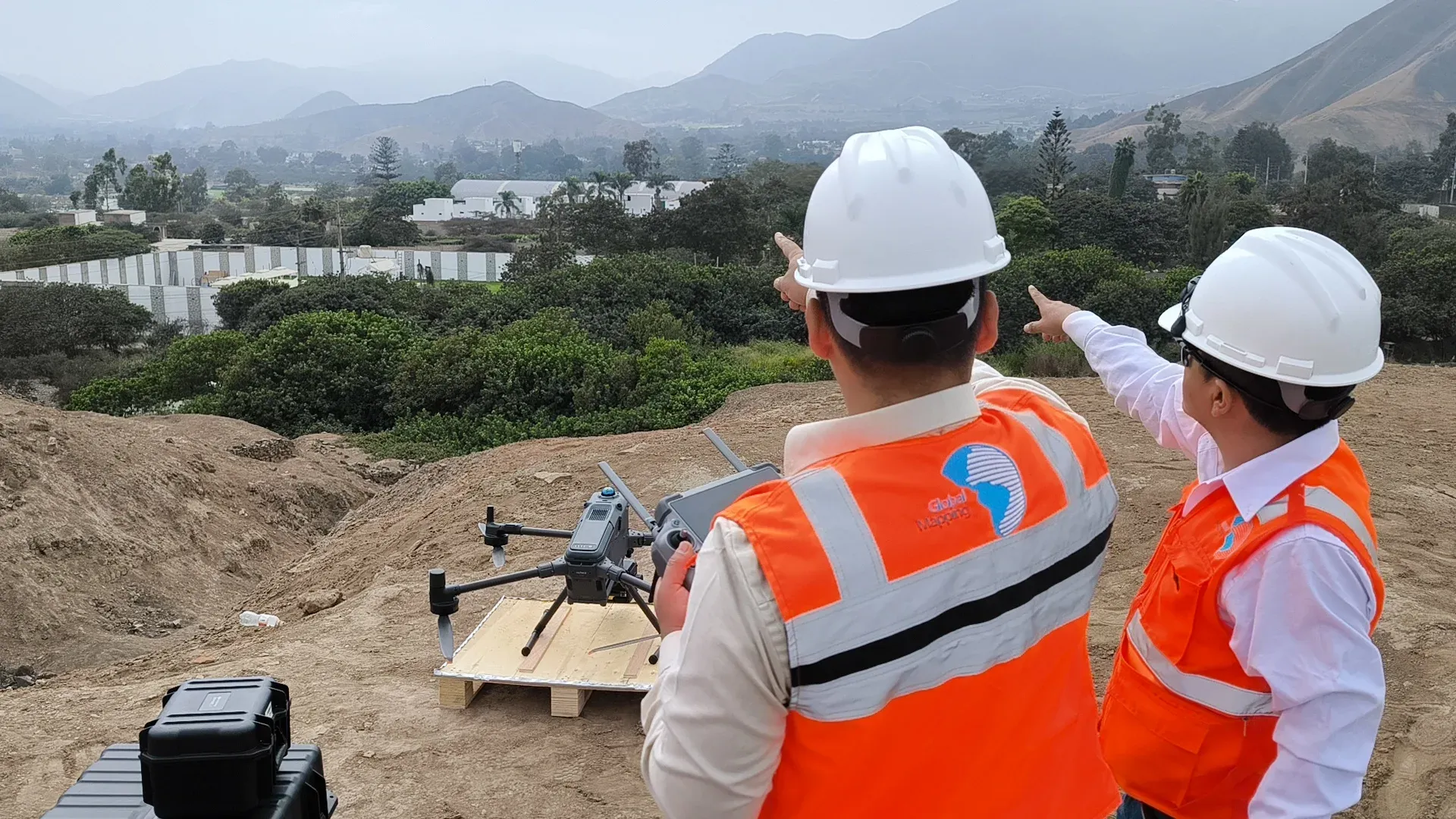 Dos especialistas de Global Mapping señalan el valle mientras uno sostiene el control de un dron posado sobre una plataforma de madera