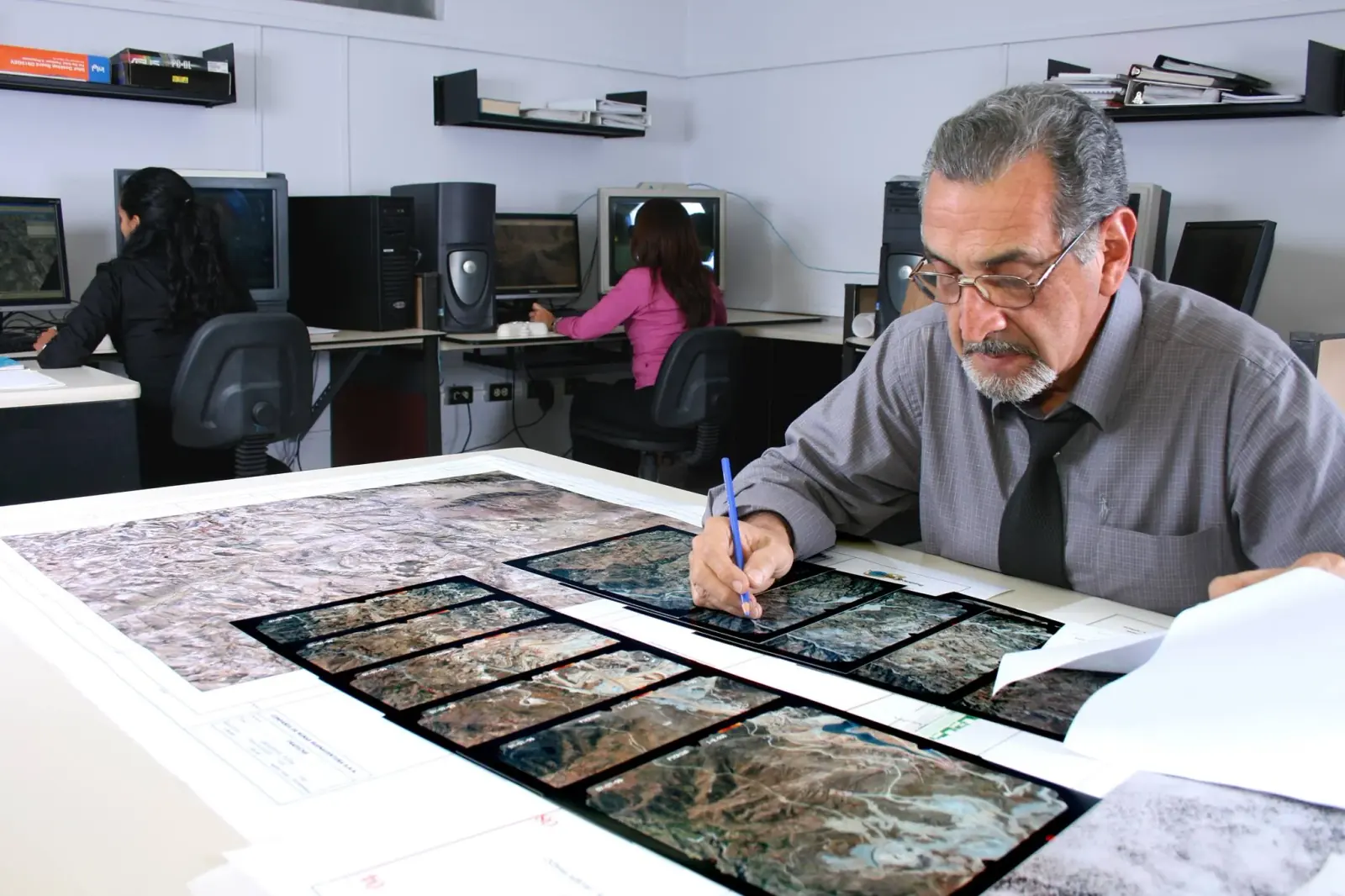 Especialista revisando fotografías aéreas en la oficina técnica de Global Mapping, con el equipo de gabinete al fondo